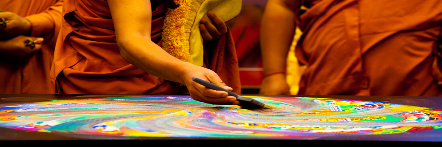 Arms of monks using a brush to mix up the sand mandala