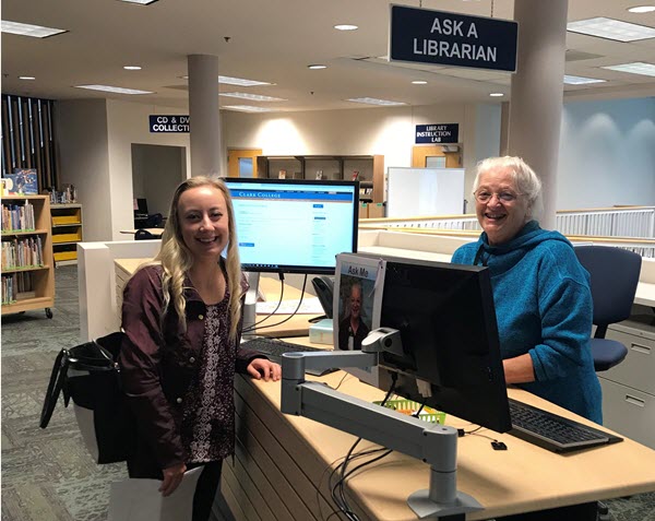 a smiling student and librarian stand across from each other at a desk labeled "Ask a Librarian"